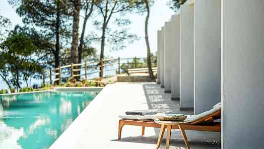 En solsäng och ett litet bord vid en pool, omgiven av pelare och träd. (AI-genererad text)