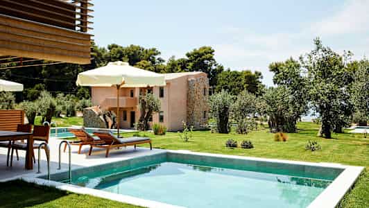 En pool omgiven av gröna gräsmattor och solstolar med parasoll, med en byggnad i bakgrunden. (AI-genererad text)