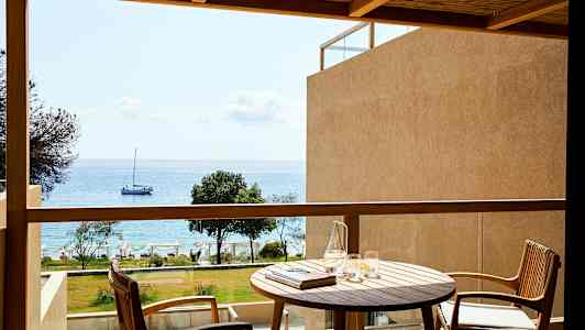 En balkong med utsikt mot havet, med ett bord och två stolar. (AI-genererad text)