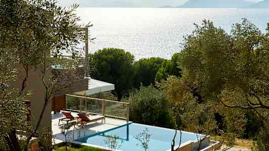 En villa med privat pool omgiven av träd med utsikt mot havet och berg i bakgrunden. (AI-genererad text)