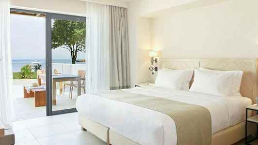 Modernt sovrum med dubbelsäng och öppning till terrass med havsutsikt. (AI-genererad text)