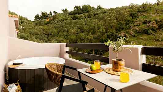 En balkong med ett spabad, ett bord med saftglas och frukt samt en utsikt över grönska. (AI-genererad text)