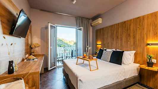 Modernt hotellrum med dubbelsäng, sittmöbler på balkongen och utsikt över en grönskande kulle. (AI-genererad text)