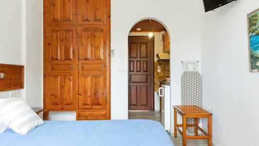 Ett rum med en säng, träskåp, strykbräda och en öppning till ett kök. (AI-genererad text)