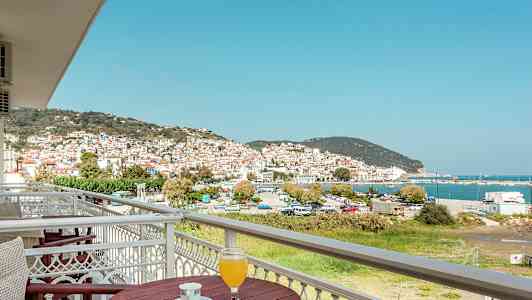 Utsikt över en stad med vita hus och röda tak, vid havet, från en balkong med bord och dryck. (AI-genererad text)