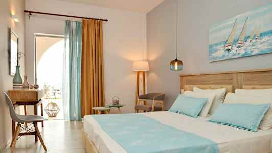 Vy av ett hotellrum med en säng, skrivbord och stolar, dekorerat med blå och gula färgtoner. (AI-genererad text)