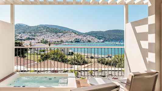 Utsikt från en terrass med två stolar och ett spabad, mot en kuststad med berg i bakgrunden. (AI-genererad text)