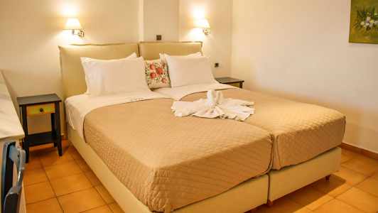 Ett hotellrum med två enkelsängar ihopställda som en dubbelsäng, täckta med beige överkast och dekorativa kuddar. Handdukar formade som en svan ligger på sängen. (AI-genererad text)