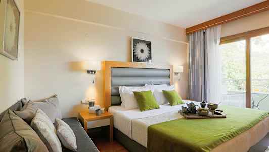 Ett hotellrum med en dubbelsäng med gröna och vita detaljer, en soffa på sidan, och ett fönster som leder till en balkong med utsikt. (AI-genererad text)