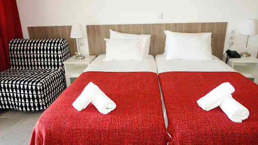 Två enkelsängar med röda överkast och vita handdukar på toppen. (AI-genererad text)