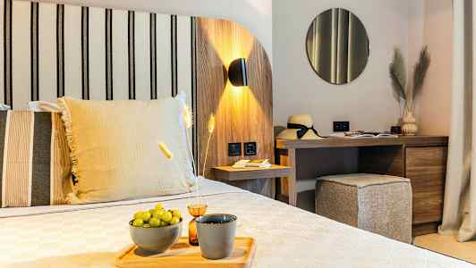 Ett modernt hotellrum med trädekor, en bädd med dekorativa kuddar, ett skrivbord med spegel och dekorativa föremål, och gröna druvor på ett fat. (AI-genererad text)