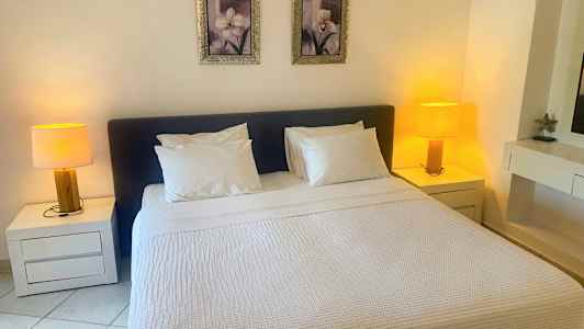 Ett sovrum med en dubbelsäng, två nattduksbord med lampor och två tavlor ovanför sängen. (AI-genererad text)