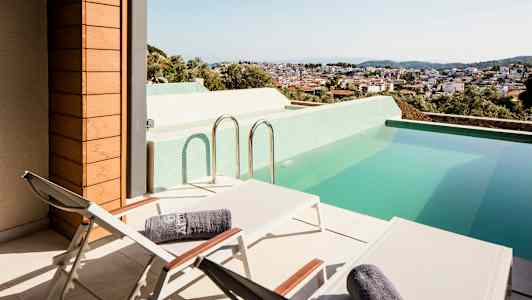 Terrass med solstolar och en pool, med utsikt över en stad. (AI-genererad text)