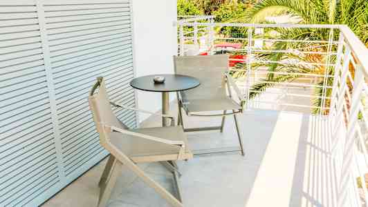 En balkong med två beige stolar och ett svart runt bord. (AI-genererad text)