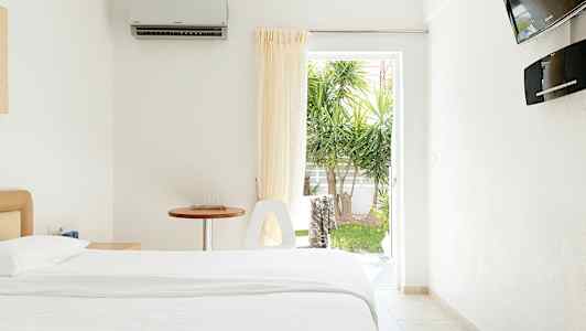 Ett ljust hotellrum med en säng, ett bord och en öppning mot en trädgård. (AI-genererad text)