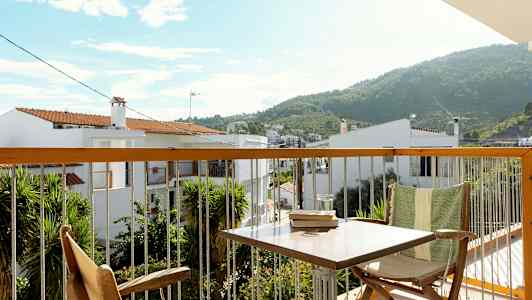 Utsikt från en balkong med möbler och grönska, samt hus och berg i bakgrunden. (AI-genererad text)