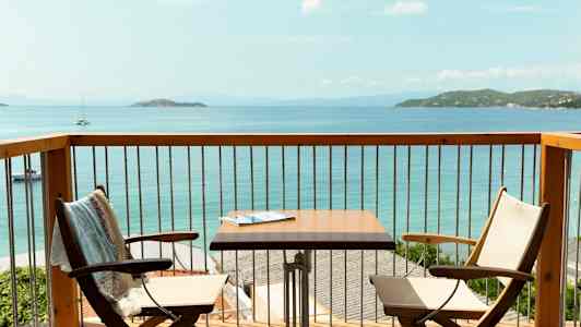 Utsikt från en balkong med två stolar, ett bord och havet i bakgrunden. (AI-genererad text)