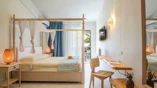 Ett hotellrum med en himmelsäng, dekorativa lampor och en skrivbordsyta med stol samt en skål med två ananaser. (AI-genererad text)