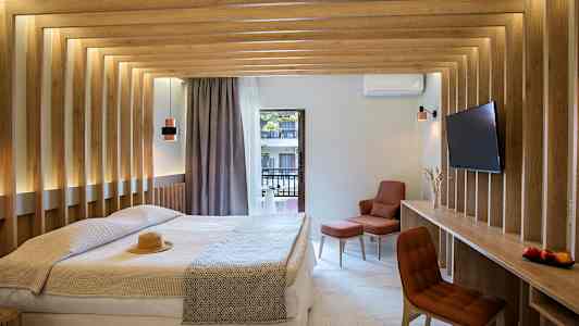 Ett modernt hotellrum med en dubbelsäng, träpaneler på väggarna, och utsikt mot en balkong. Rummet har en tv och en bekväm sittplats. (AI-genererad text)