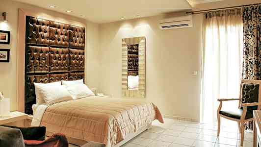 Ett sovrum med en dubbelsäng, ett stort vadderat huvudgavel och en spegel på väggen. (AI-genererad text)