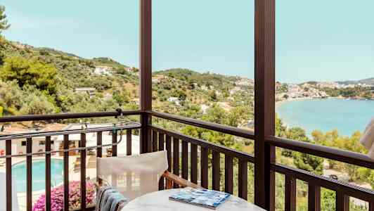 Utsikt från en balkong med bord och stol mot en pool, grönska och havsfjord. (AI-genererad text)