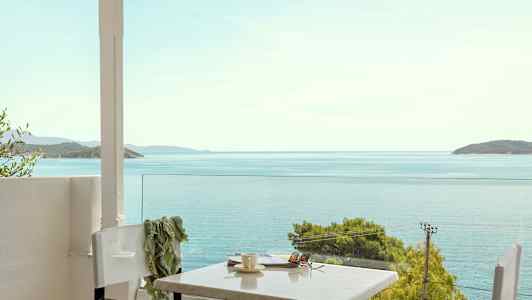 Utsikt mot havet från en terrass med bord och stolar. (AI-genererad text)