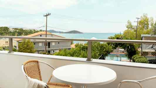 En balkong med ett litet bord och två stolar, med utsikt över en pool och havet. (AI-genererad text)