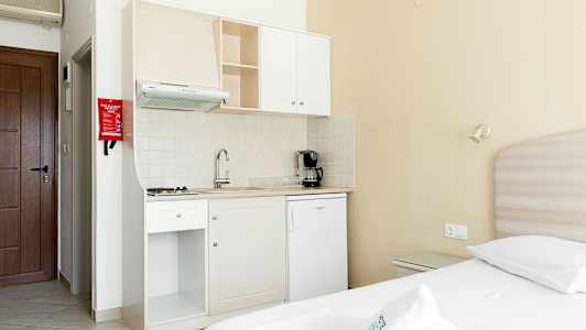 Liten kökspentry med vit köksinredning i ett rum med en säng. (AI-genererad text)