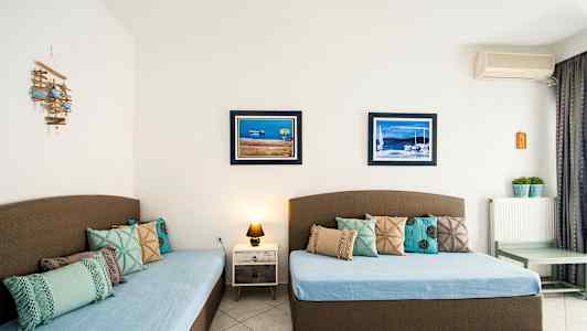 Två sängar med blå överkast och dekorativa kuddar, två tavlor med marina motiv på väggen. (AI-genererad text)