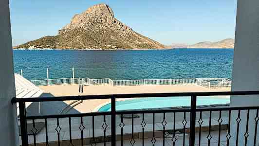 Bilden visar utsikten från en balkong över en pool och hav, med en bergig ö i bakgrunden. (AI-genererad text)