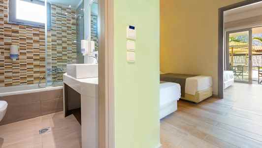 Utsikt mot ett badrum med kakelväggar och ett angränsande sovrum med sängar. (AI-genererad text)