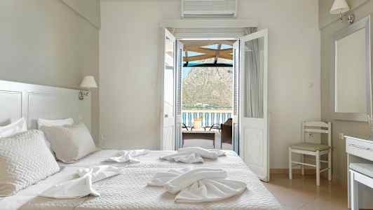 Ett hotellrum med en säng, stolar och ett bord med en utsikt genom dörrar mot balkongen och berg i bakgrunden. (AI-genererad text)