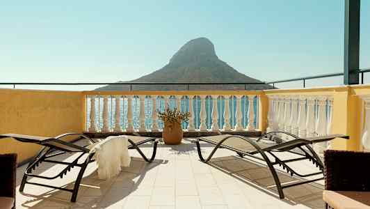 Terrass med solsängar och utsikt över havet och en liten bergformation. (AI-genererad text)