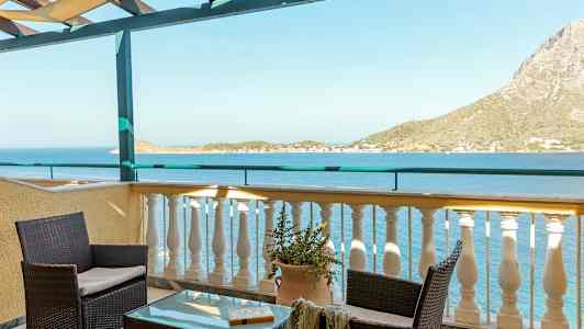 Utsikt från en terrass med bord och stolar som vetter mot havet och en bergig kust. (AI-genererad text)