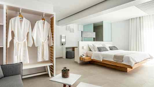 Bild av ett elegant hotellrum med en stor säng, vita badrockar hängande i en garderob och ljusa moderna möbler. (AI-genererad text)