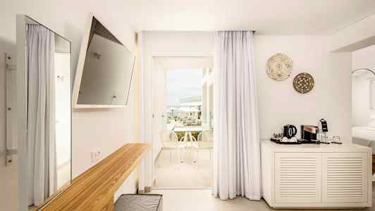 Ett modernt hotellrum med ljus inredning, en TV på väggen, ett skrivbord och en balkong med utsikt. (AI-genererad text)