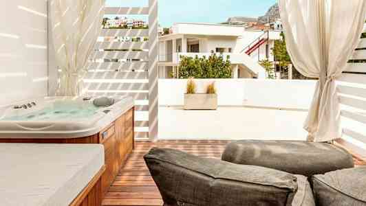 Bilden visar en terrass med en jacuzzi, solstolar och utsikt över grannbyggnaden. (AI-genererad text)