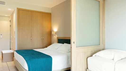 Hotellrum med dubbelsäng och enkelsäng, samt träskjutdörr. (AI-genererad text)