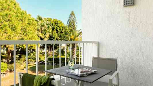 En balkong med ett bord och stolar, med utsikt över en trädgård med palmer. (AI-genererad text)