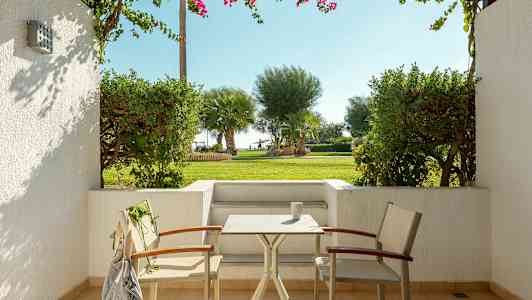 En uteplats med två stolar och ett bord, övergången till en grön trädgård med palmer i bakgrunden. (AI-genererad text)