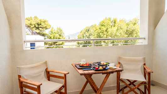 Två stolar och ett bord med frukost serverad på en balkong med utsikt över träd. (AI-genererad text)