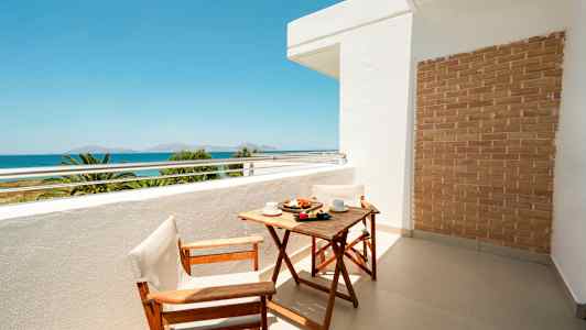 Balkong med träbord och två stolar, havsutsikt i bakgrunden. (AI-genererad text)