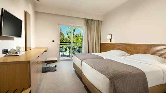 Ett hotellrum med två sängar, en arbetsbänk och en balkong med utsikt. (AI-genererad text)