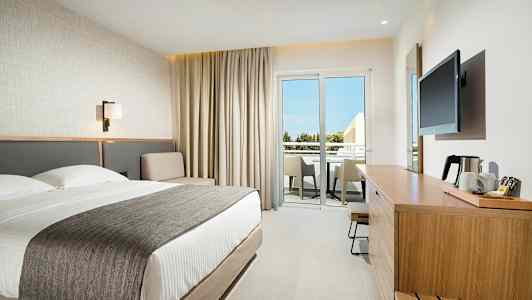 Modern hotellrum med dubbelsäng, sittgrupp och möblerad balkong. (AI-genererad text)