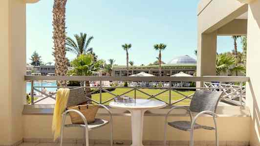 Utsikt från balkongen mot en trädgård med palmer och en pool. (AI-genererad text)