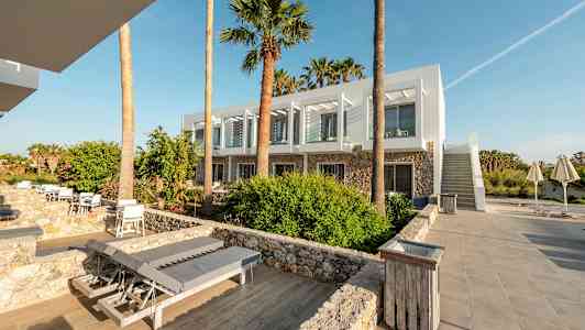 Ett modernt hotell med vita fasader och stora fönster omgivna av palmer och stenbelagda gångar. (AI-genererad text)