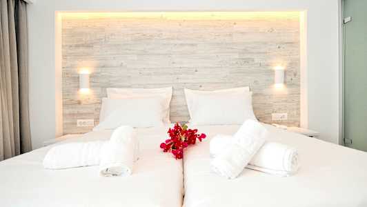 En vit bäddad dubbelsäng med röda blommor och hopvikta handdukar på toppen. (AI-genererad text)