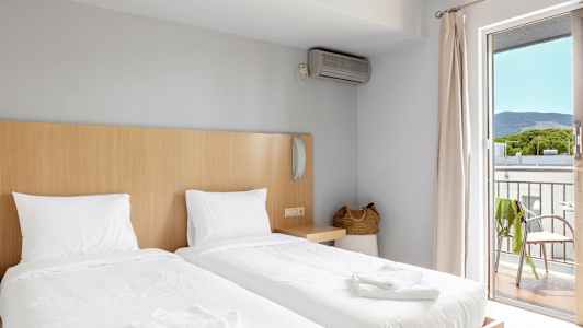 Ett hotellrum med två enkelsängar, en basket handväska, och en balkong med utsikt. (AI-genererad text)