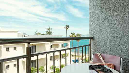 Utsikt från en balkong mot stranden med havet och palmer i bakgrunden. (AI-genererad text)