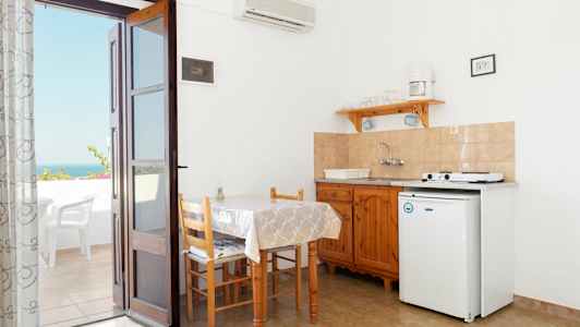 En liten köksvrå med bord, stolar och en kokvrå. En dörr leder ut till en terrass med utsikt. (AI-genererad text)